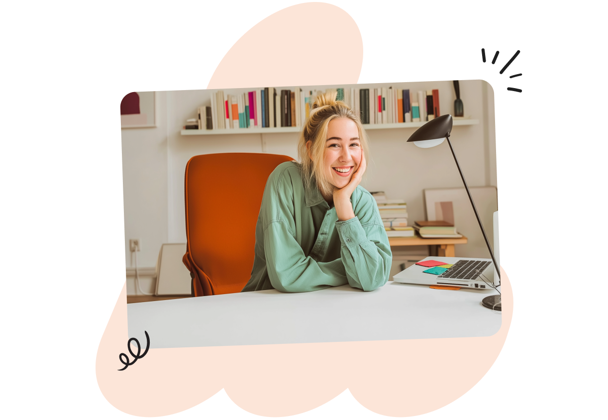 Smiling person in a green shirt sits at a desk with a laptop, surrounded by books, under a desk lamp in a cozy, well-lit room.