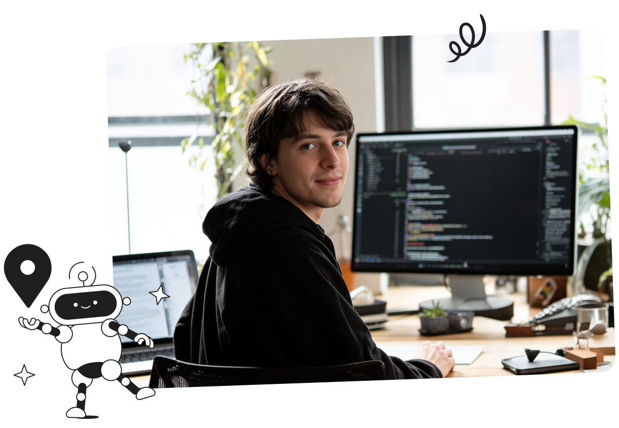 A person in a black hoodie sits at a desk with dual monitors displaying code, looking over their shoulder. Office plants and a window are in the background.