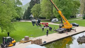 A large horse sculpture is being lifted by a crane in a park, surrounded by workers and vehicles.