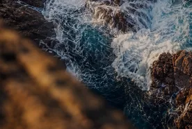 Waves crashing against rugged brown rocks with foamy white water in a vivid, turbulent sea.