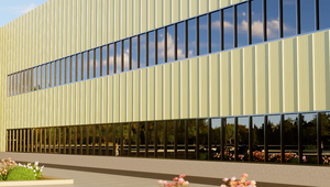 Modern building with vertical yellowish panels and large reflective windows, surrounded by landscaped flowers and trees.