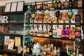 Bar shelf with assorted liquor bottles, glasses, and decorative signs. Various types of alcohol displayed in an organized fashion.