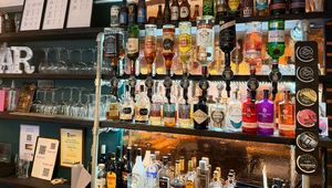 Bar shelf with assorted liquor bottles, glasses, and decorative signs. Various types of alcohol displayed in an organized fashion.