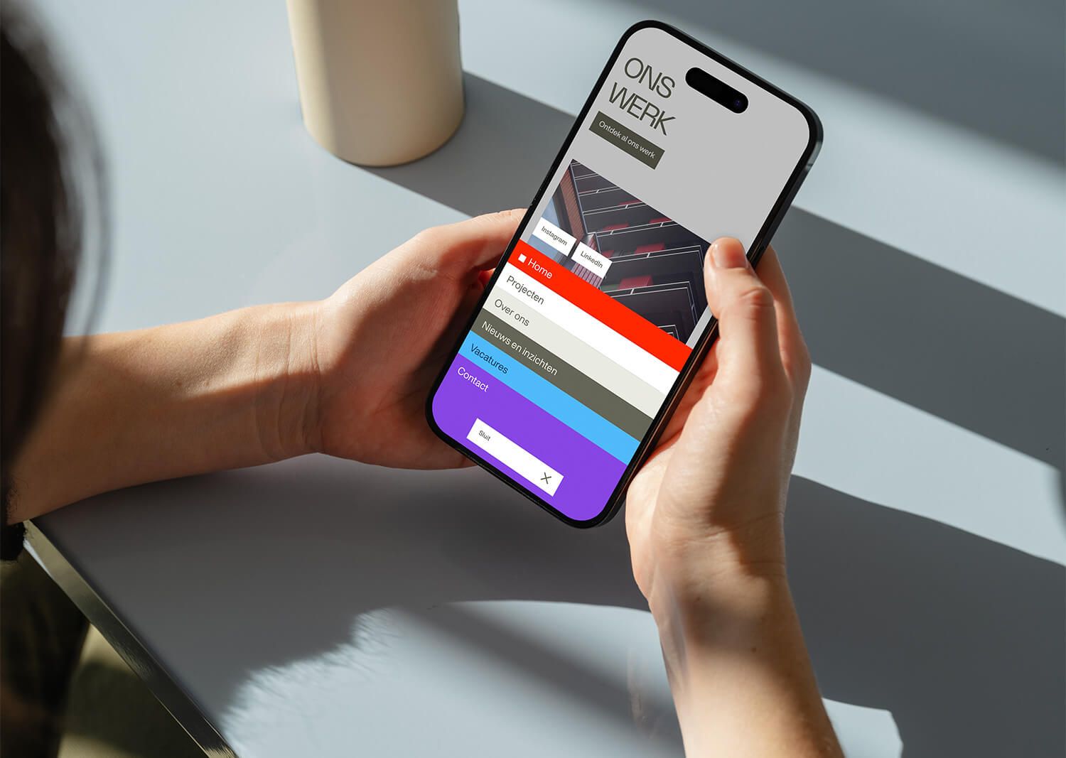 Person holding a smartphone displaying a colorful menu screen titled "ONS WERK," with several navigation options visible.