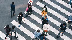 Aerial view of people crossing a wide zebra-striped crosswalk on a busy street, with individuals walking in various directions.