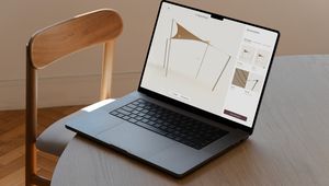A laptop on a wooden table displaying a design application with a canopy structure, next to a wooden chair on a wooden floor.