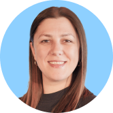 Smiling person with long brown hair, wearing a black top, against a light blue background.