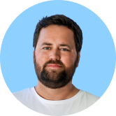 A man with a beard and short hair in a white shirt, against a light blue background, looking at the camera.