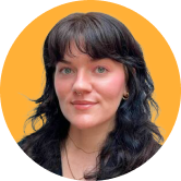 Woman with dark hair and bangs, wearing earrings and a necklace, against an orange background, smiling gently.
