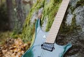 A green electric guitar with a unique body shape rests against a moss-covered rock in a forest, surrounded by fallen leaves.
