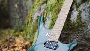 A green electric guitar with a unique body shape rests against a moss-covered rock in a forest, surrounded by fallen leaves.