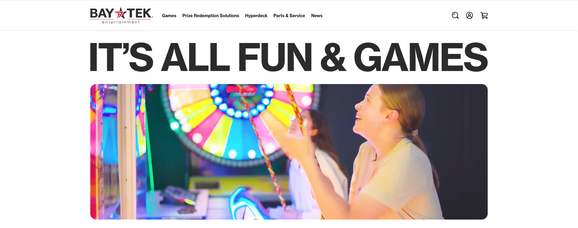 Two people smiling and playing an arcade game under vibrant neon lights, with a large spinning wheel in the background.