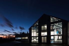 Modern building with large windows illuminated at dusk, showcasing interior details against a clear evening sky.