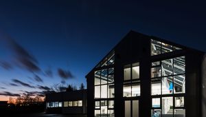 Modern building with large windows illuminated at dusk, showcasing interior details against a clear evening sky.