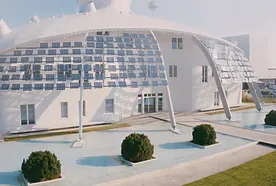 Futuristic white building with solar panels and curved design, surrounded by a shallow pool and neatly trimmed bushes.