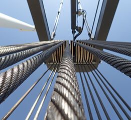 Close-up view of multiple steel cables extending upwards, connected to a pulley system against a clear blue sky.