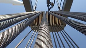Close-up view of multiple steel cables extending upwards, connected to a pulley system against a clear blue sky.