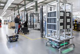 Automated robots transporting storage bins in a modern warehouse, with workers operating machinery in the background.