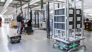 Automated robots transporting storage bins in a modern warehouse, with workers operating machinery in the background.
