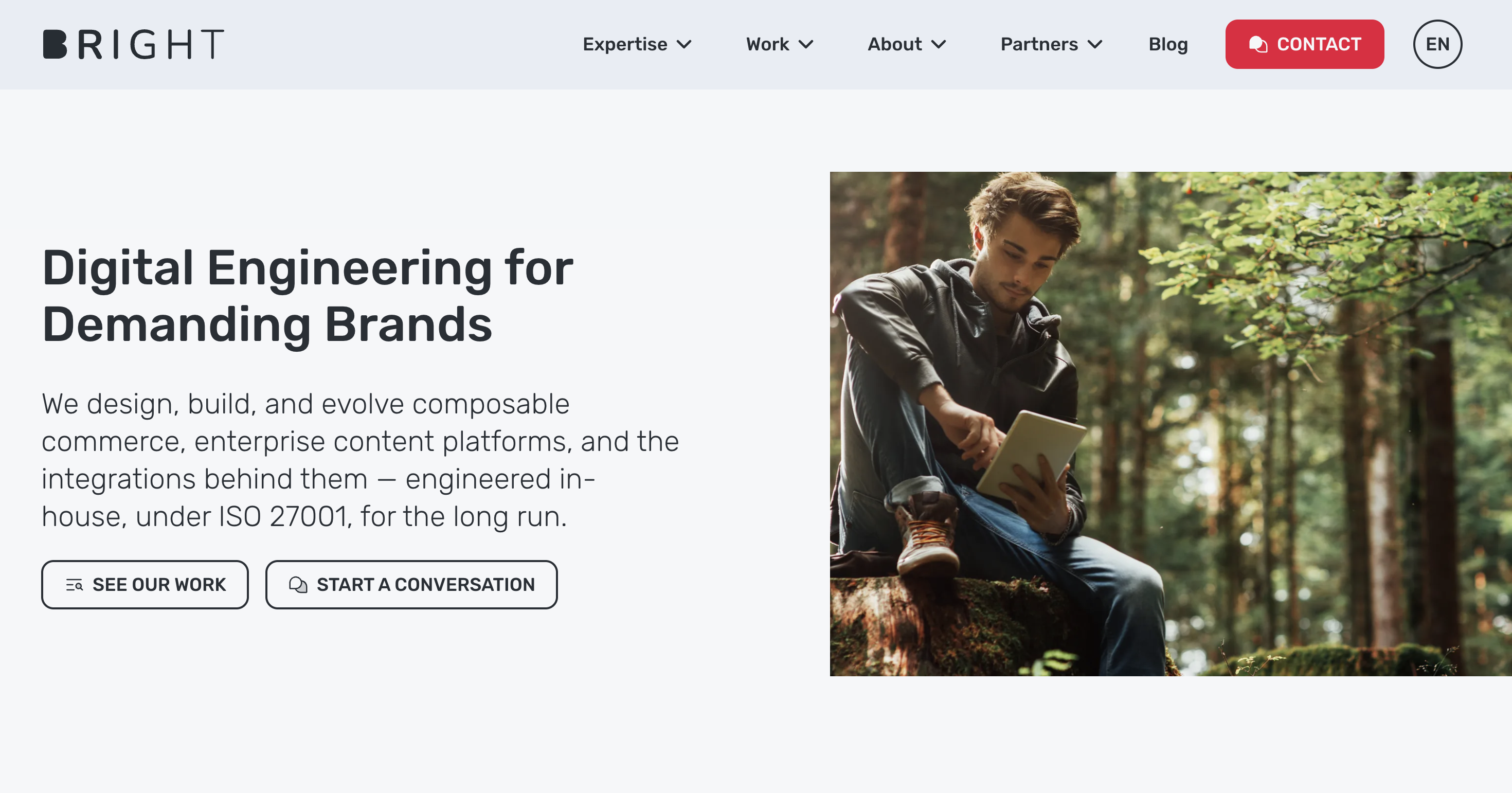 Man sitting in a forest using a tablet next to text about digital engineering services for brands, with contact options above.