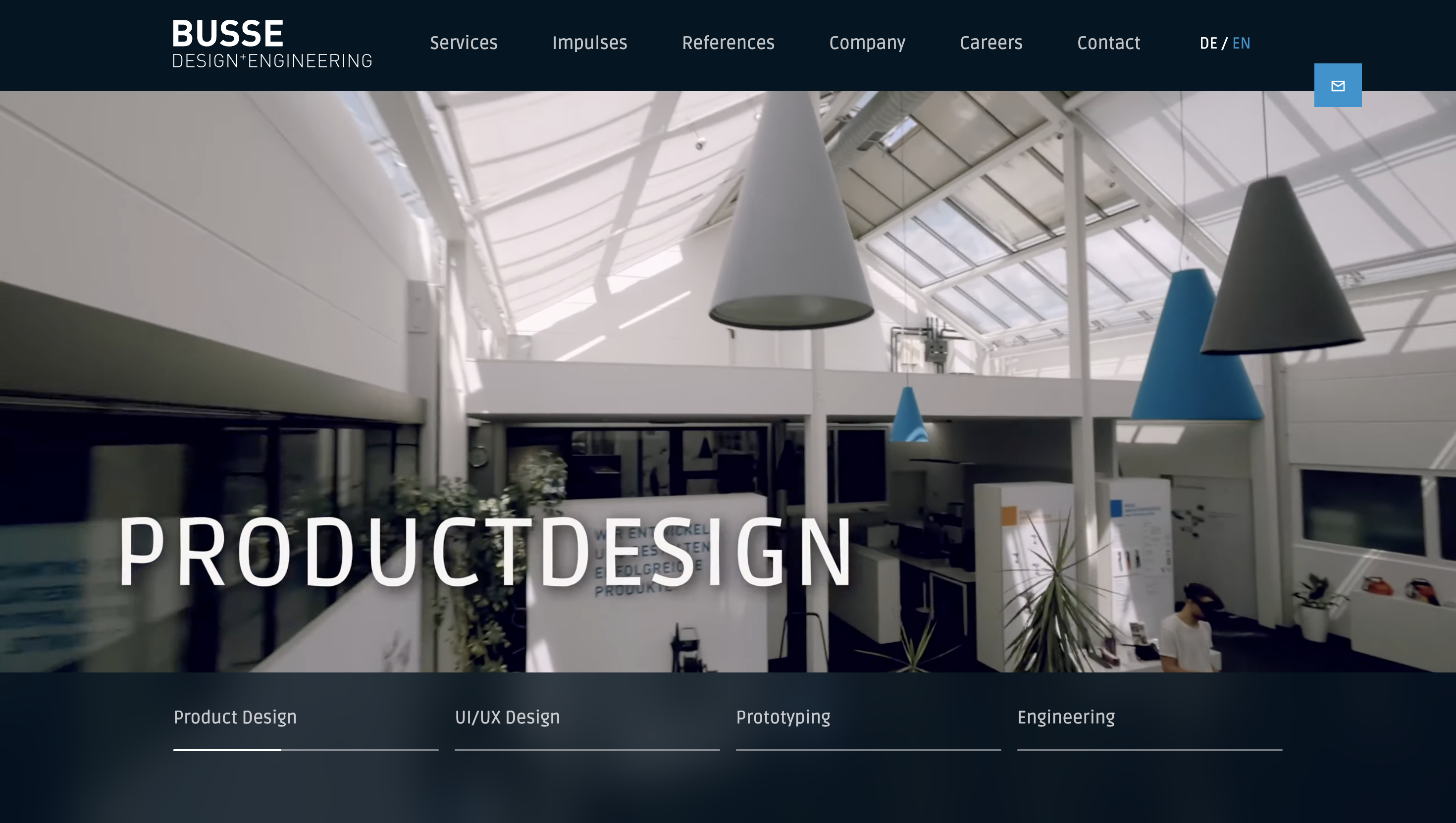 Modern office interior with high ceilings, large hanging light fixtures, and the word "Productdesign" prominently displayed.