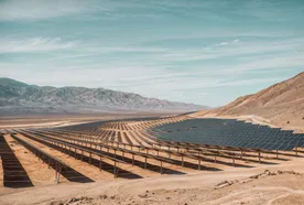 Expansive solar panel field in a desert landscape with mountains in the background under a clear blue sky.