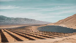 Expansive solar panel field in a desert landscape with mountains in the background under a clear blue sky.