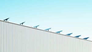 Rooftop with solar panels above a corrugated metal wall against a clear blue sky.