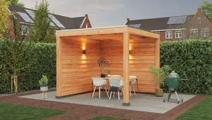 Wooden gazebo on a patio with a table, chairs, and a grill. Surrounded by a hedge, under a cloudy sky with neighboring houses in the background.