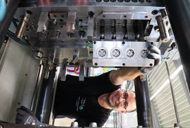 A technician smiles while adjusting a large industrial machine in a manufacturing facility.