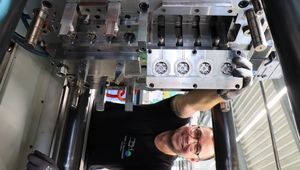 A technician smiles while adjusting a large industrial machine in a manufacturing facility.