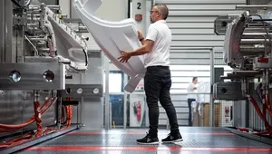 A worker in a factory operates a large machine, handling a curved, white plastic component in an industrial setting.