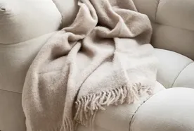 A soft beige throw blanket with fringes draped over a plush, light-colored sofa, creating a cozy and inviting atmosphere.