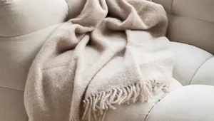 A soft beige throw blanket with fringes draped over a plush, light-colored sofa, creating a cozy and inviting atmosphere.