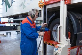 A mechanic in blue coveralls uses a power tool to work on a truck wheel in a garage.