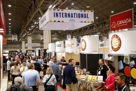 People attending a bustling international trade show with various booths, including one labeled "Canada" and another showcasing bakery products.
