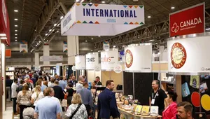 People attending a bustling international trade show with various booths, including one labeled "Canada" and another showcasing bakery products.