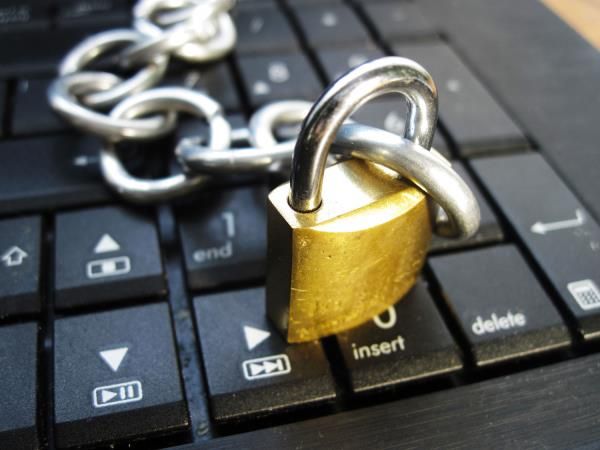 A silver chain with a gold padlock is draped across a black computer keyboard.