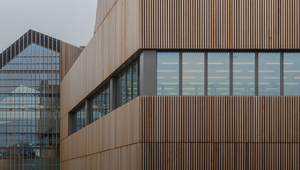 Modern building with wooden paneling and large windows, featuring "UEA" on the facade. A person walks along a pathway beside it.