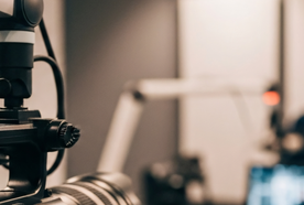 Close-up of a professional camera in a modern recording studio, with a blurred background featuring a microphone and a computer screen.