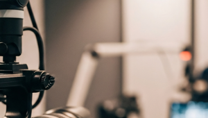 Close-up of a professional camera in a modern recording studio, with a blurred background featuring a microphone and a computer screen.