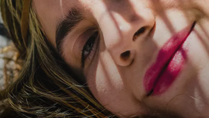 Close-up of a person's face, partially shaded by light patterns, with vibrant pink lips and a relaxed expression.