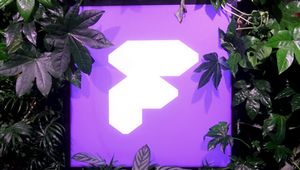 A purple sign with a white geometric logo is surrounded by lush green foliage.