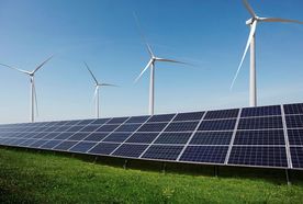 Solar panels and wind turbines on a grassy field under a clear blue sky, illustrating renewable energy sources.