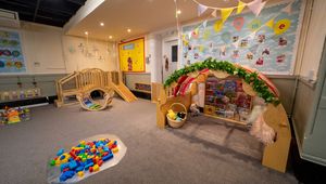 Bright and welcoming playroom with wooden slide, colorful blocks, books, and playful decorations on walls and ceiling.
