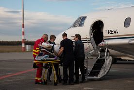 Medical staff assist a patient on a stretcher as they board a REVA air ambulance plane on an airport runway.