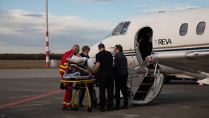 Medical staff assist a patient on a stretcher as they board a REVA air ambulance plane on an airport runway.