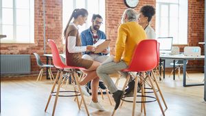 A group of professionals sit in a bright office, reviewing documents and discussing ideas together.
