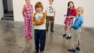 Five children standing in a room, holding strings in a star pattern, wearing colorful outfits and looking in different directions.