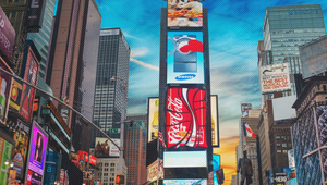 Times Square, New York City, with vibrant billboards and a bustling crowd under a blue sky with clouds.